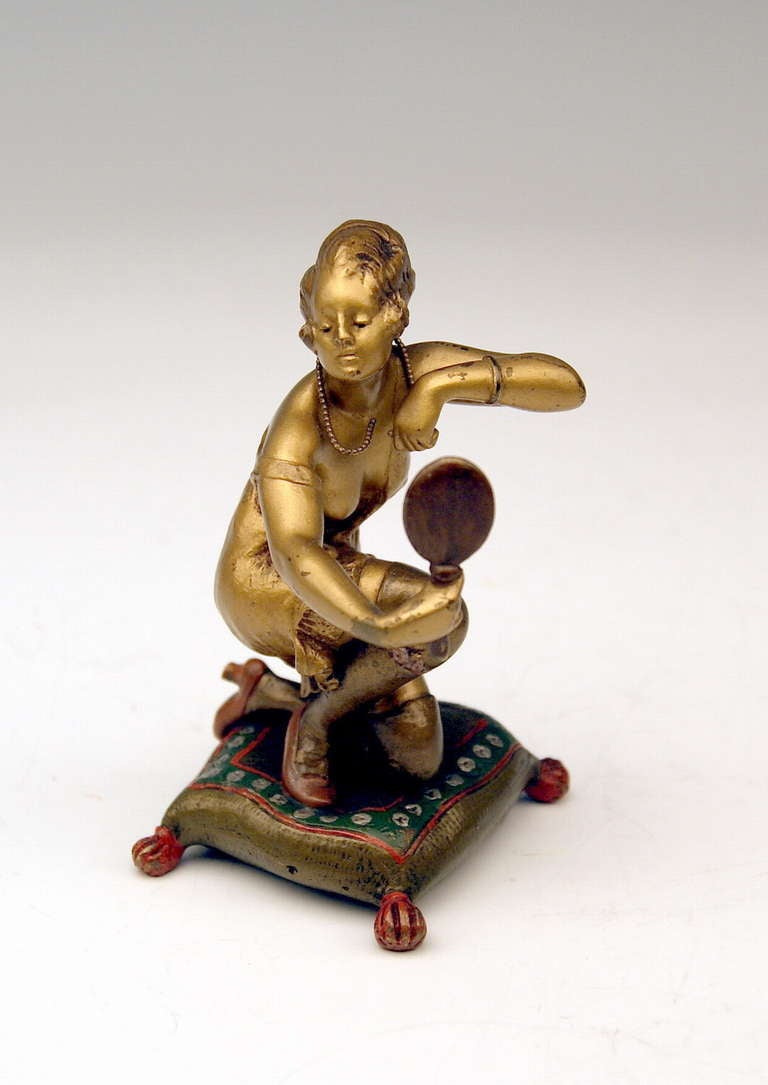A finest Viennese Late Art Nouveau Bronze / woman's figurine designed by famous modeller Bruno Zach (1891 - 1935): The barebreasted woman kneels on a cushion, seeming to view at her necklace in mirror held by right hand. The figurine is attached to