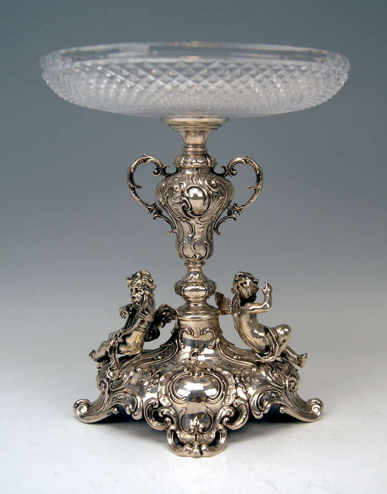 EXCELLENTLY SCULPTURED CENTREPIECE BEING ABUNDANTLY DECORATED: THE GLASS PLATTER WHICH IS ORNAMENTED WITH CUT DECORATIONS (SO-SAID DIAMOND CUT) IS ATTACHED TO STALK ORNAMENTED WITH CARTOUCHES AS WELL AS WITH A PAIR OF HANDLES. - THE MASSIVE BASE IS