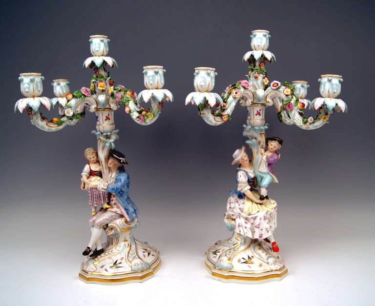 Each of the candlesticks has  FIVE grommets /  there are FIVE ARMS existing, being abundantly decorated with sculptured flower's blossoms and fruits. - The stalk consists of SCULPTURED PAIR OF FIGURINES - these are:
  - a lady having sat down,