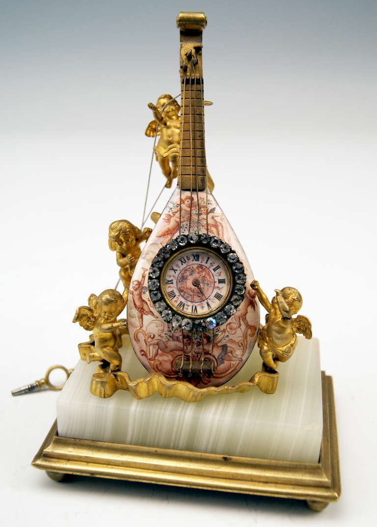 Gorgeous Viennese bronze table clock, looking like as following:
The clock is shaped as mandolin with strings  /  the clockface with Roman numerals is edged by border made of cut glass stones  /  the clock's surface is painted with enamel,
