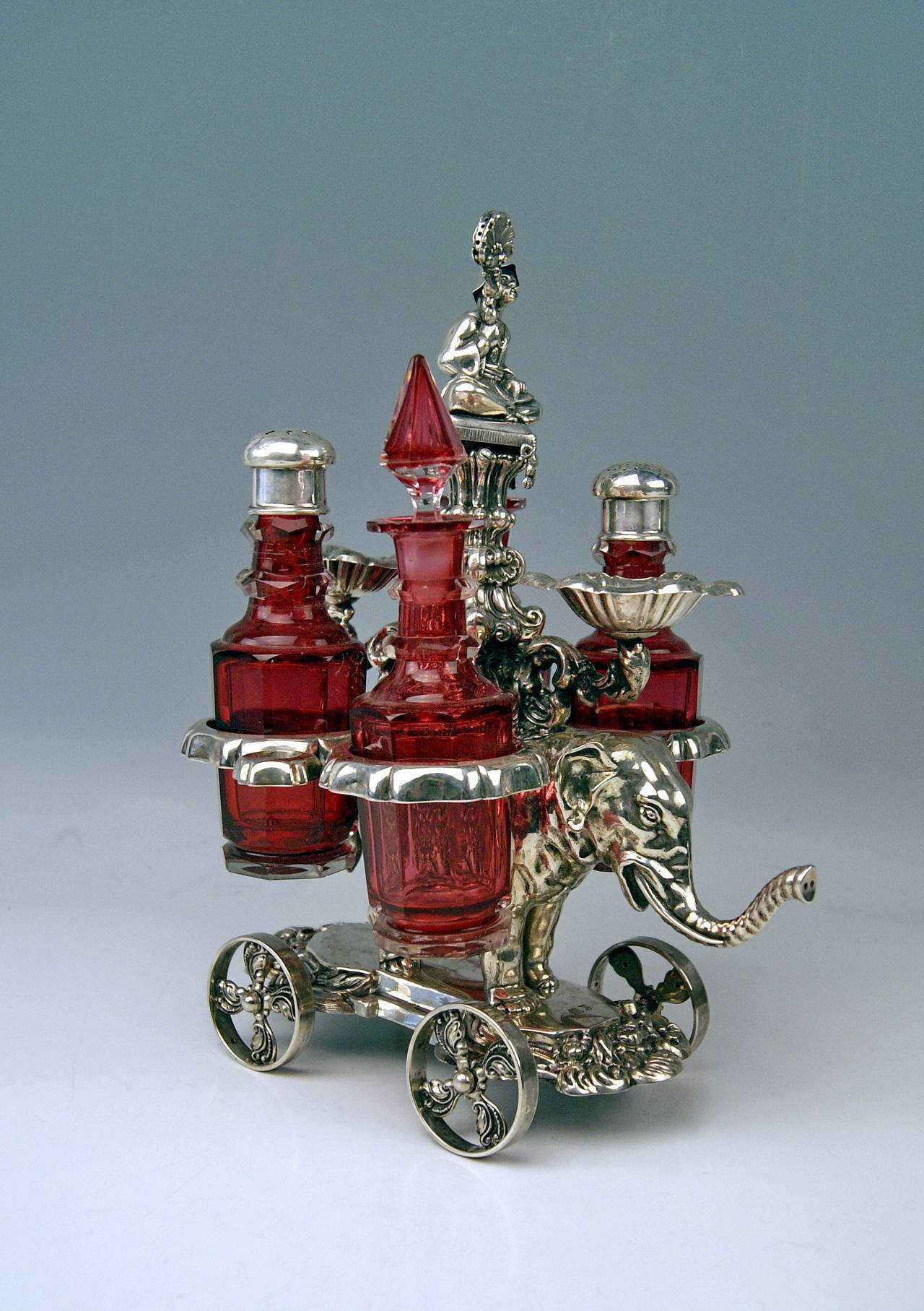 Gorgeous Rarest Condiment Set, consisting of Silver Holder / Support with Glass Bottles  /  made in Vienna.

PARTICULAR FEATURE:
The silver holder keeping the bottles is shaped as a sculptured elephant's figurine attached to wheels which are in