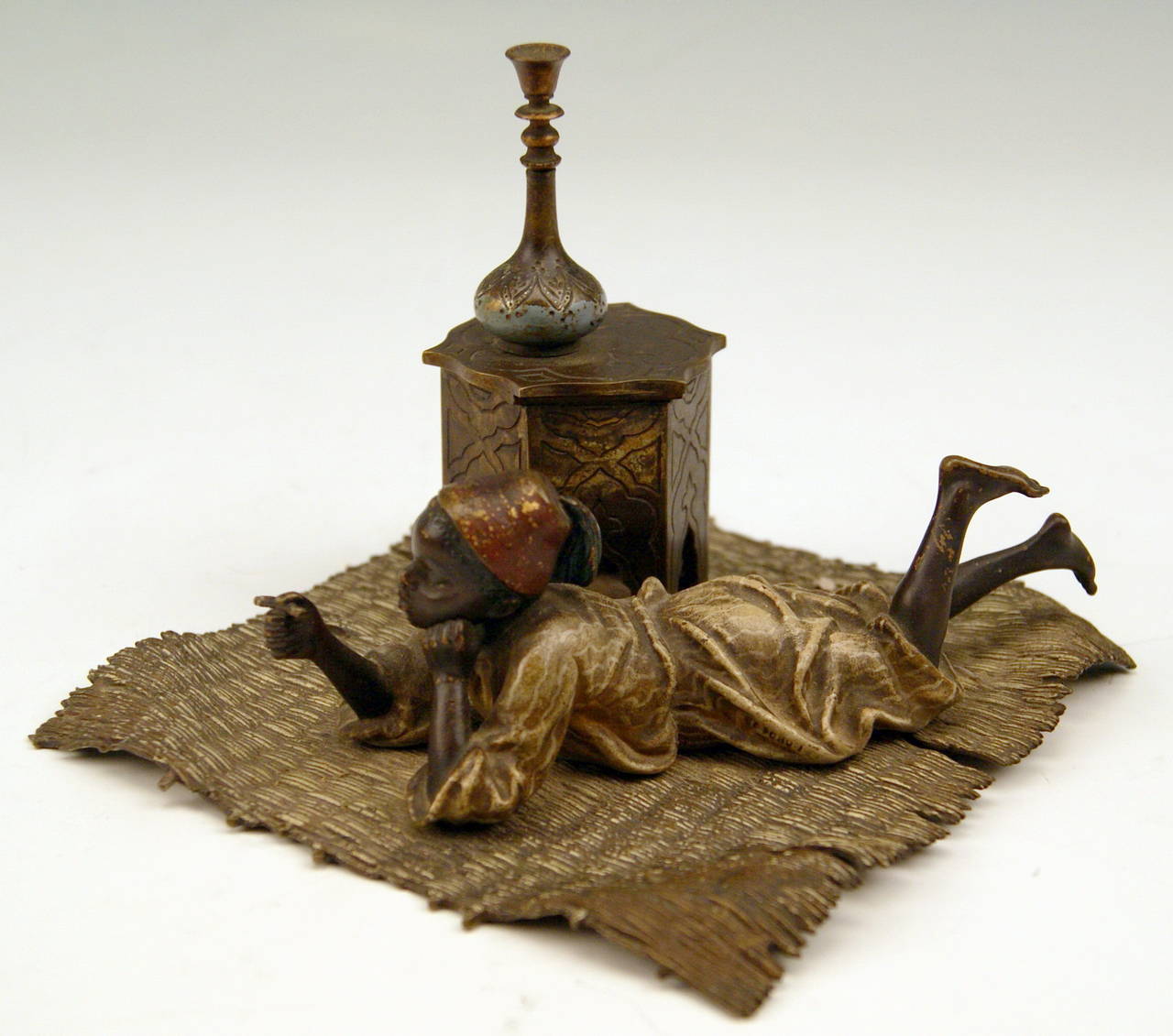 Gorgeous Vienna Bronze figurine made by famous manufactory Ber(g)man(n)  circa  1900. 
 The Arab boy - lying prone on a wattled carpet  -  wears the characteristic fez / tarboosh  as well as Arab garments. He smokes a cigarette, having the legs