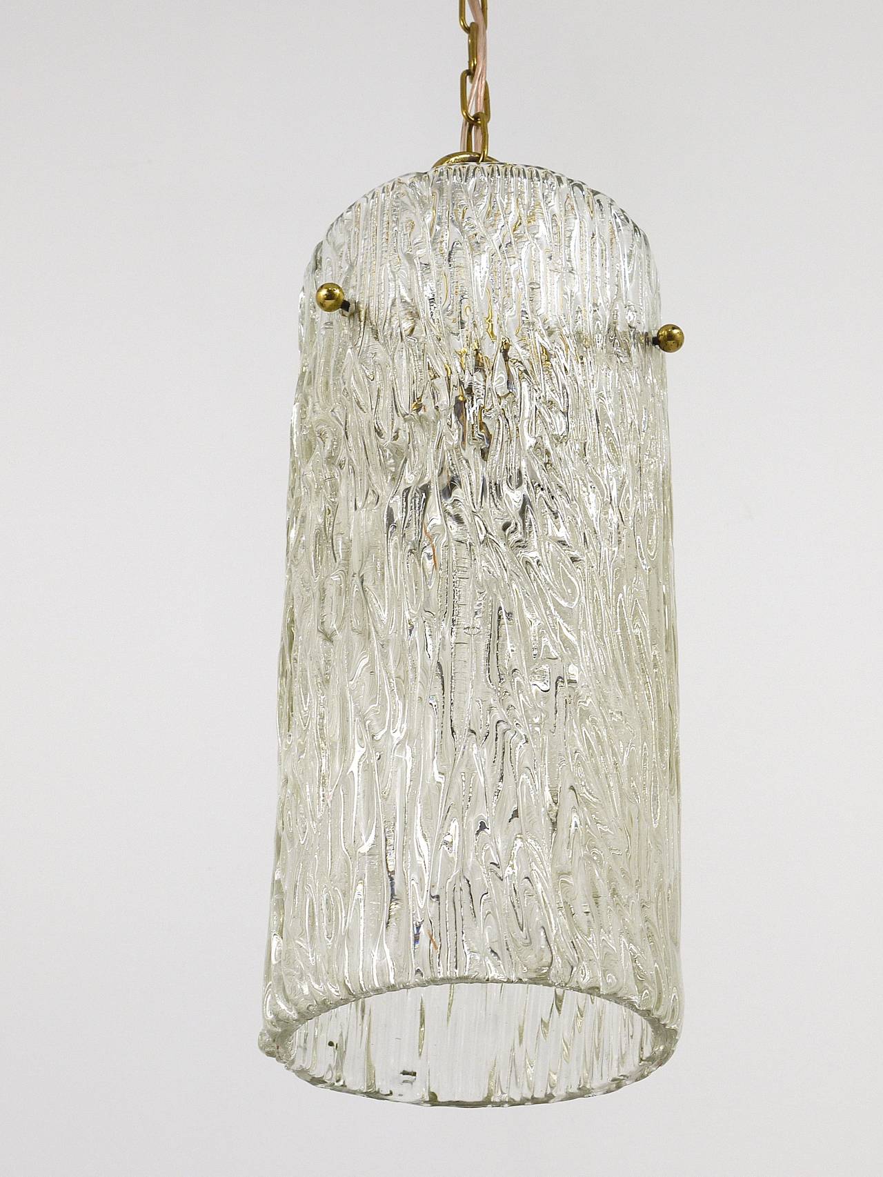 Up to two beautiful matching pendant lamps from the 1950s, designed an executed by J.T. Kalmar in Austria. Sold and priced per piece. Brass hardware with a big tube made of clear textured melting glass. In good condition with nice patina on the