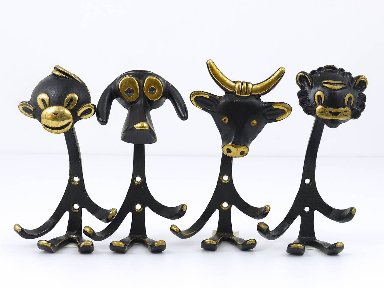 A set of 4 Viennese modernist brass wall coat hooks, displaying a dog, a cow, a lion and a monkey. Designed in the 1950s by Walter Bosse, executed by Baller Vienna. Made of black finished brass. In very good condition with nice patina. Each hook has