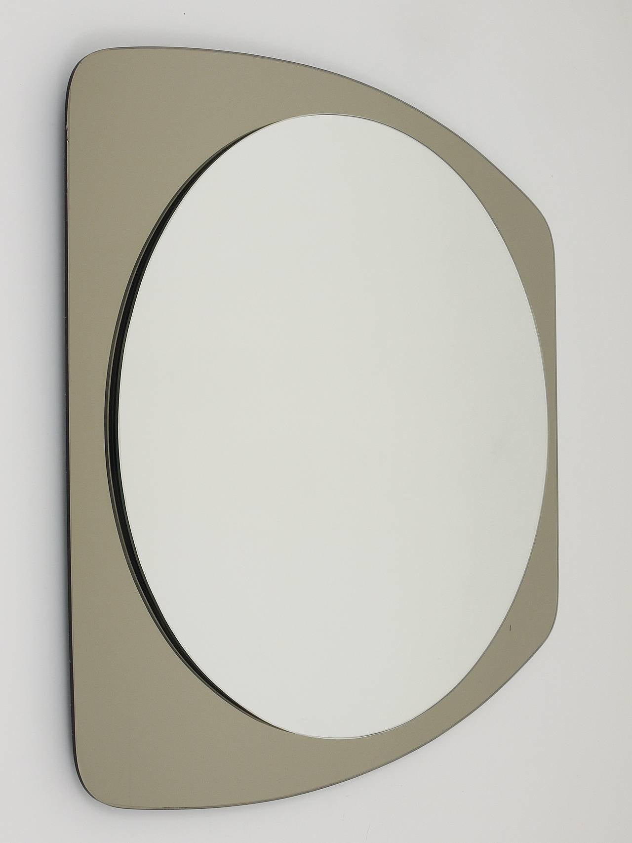 A beautiful double-levelled wall mirror from the 1970s, made in Italy by Cristal Arte / Crystal Arte. Oval mirror with a grey smoked rectangular backplate glass with rounded corners. Excellent condition, please notice that there is a little spot on