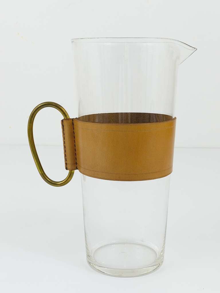 A beautiful glass pitcher with leather belt and brass handle, designed and executed by Viennese Modernist Carl Aubock. Very rare item, because of its size. Height: 11 1/4