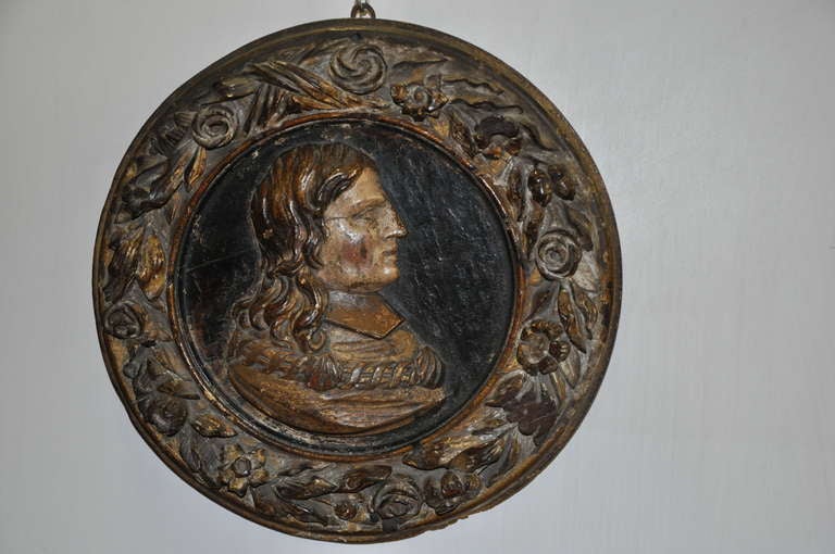A 17th c. carved and lacquered  relief , depicting a male profile with a collar showing a shell, probably to symbolize the membership of an equestrian order.
The frame and the relief are carved from the same piece of wood.
The frame is decorated