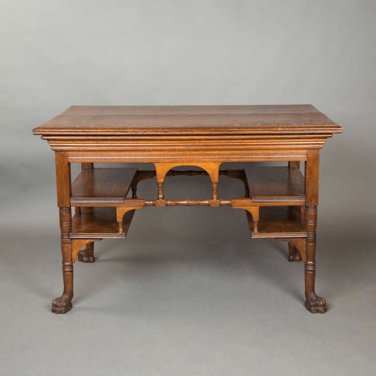 A victorian oak centre table circa 1870, in the manner of Alfred Waterhouse. Of quartersawn oak, the four-plank top with richly moulded frieze above four shelves on paw-footed legs