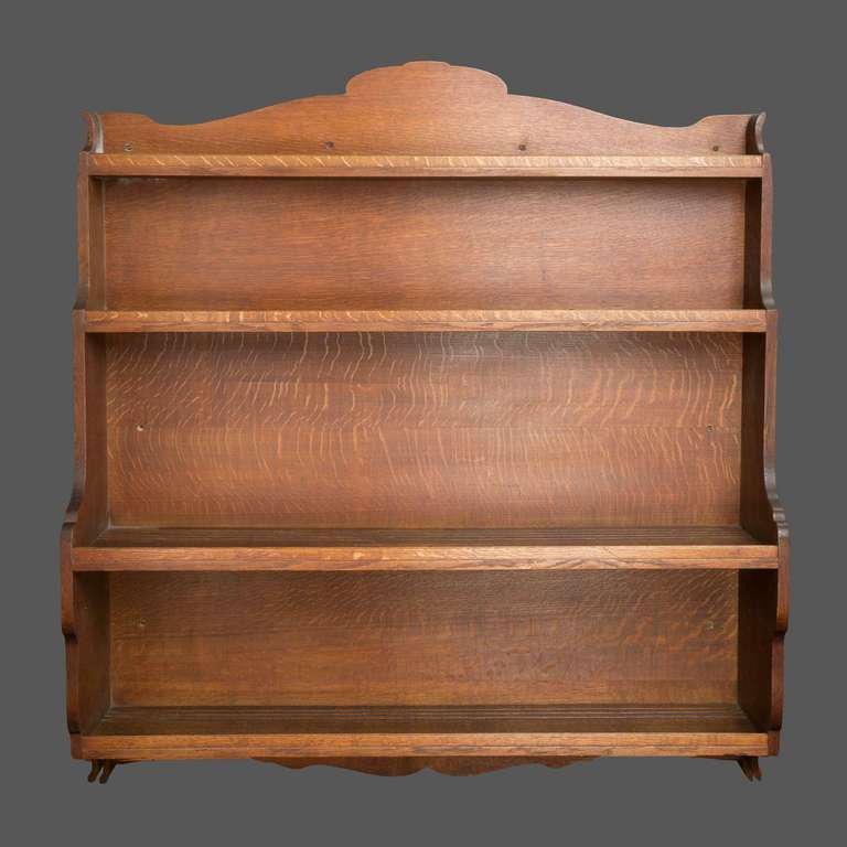 An oak hanging wall shelf, designed by Sir Robert Lorimer, with four channelled shelves.  Shaped top with scrolled sides and a similar apron.  Theses hanging shelves , a traditional form found in Scottish cottage kitchens were almost certainly made