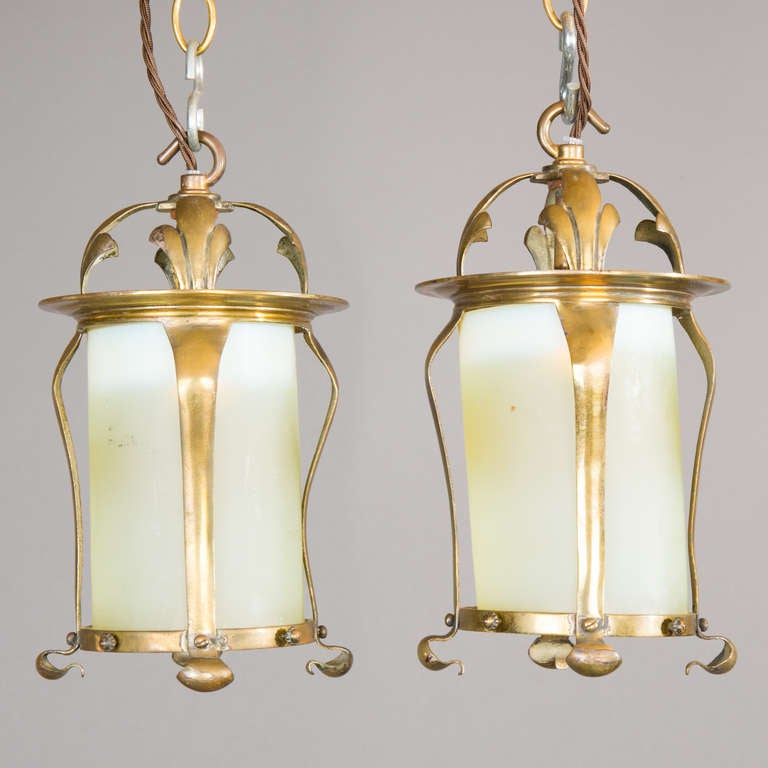 In the manner of W.A.S. Benson, a pair of Arts & Crafts brass and vaseline glass hanging lanterns, the cylindrical glass shades within scrolling brass frames. Electrified for the UK