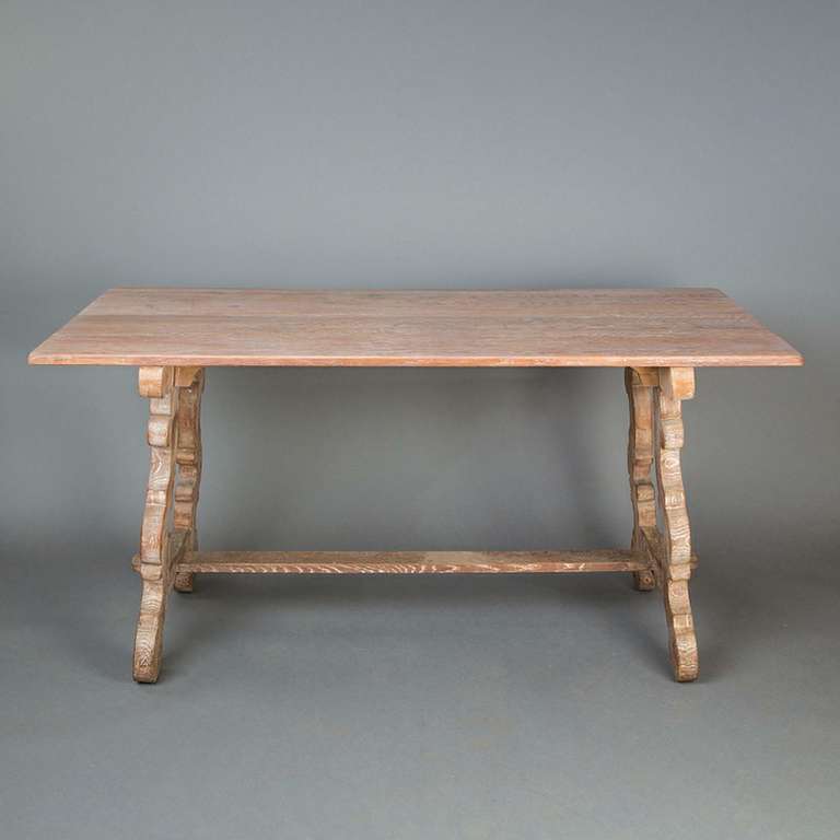 A Scottish arts and crafts, Tuscan style limed oak table, circa 1920, in the manner of Sir Robert Lorimer with scrolled trestle supports joined by a stretcher.