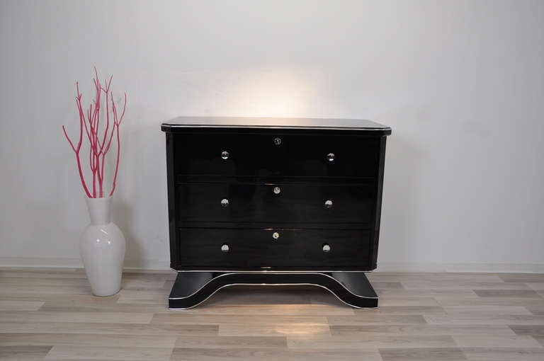 Beautiful black commode or dresser with an elegant design and wonderfully shaped foot. It features high gloss black piano lacquer with a mirror finish and three chromed knobs on each of the three drawers. It also got refined with luxurious chrome