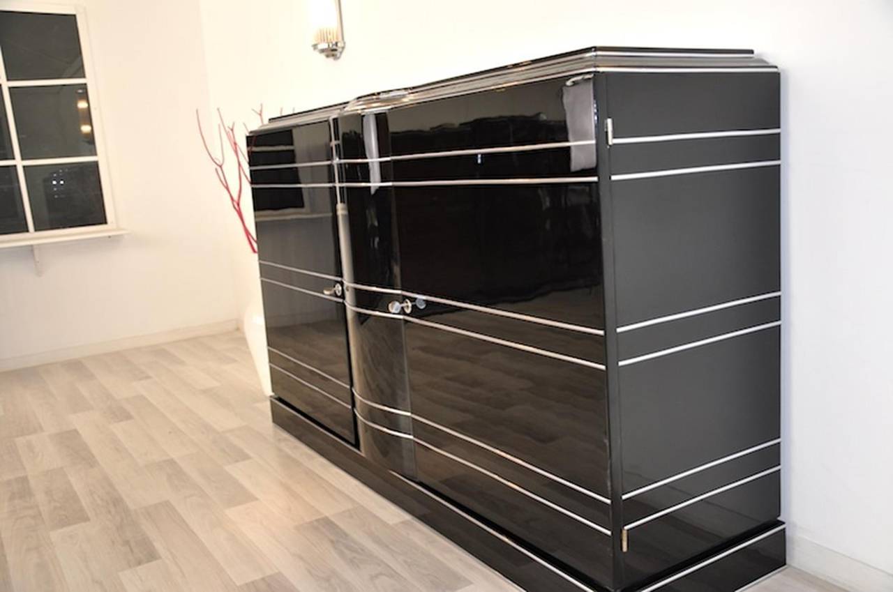 Art Deco style sideboard with elegant chrome bars. A unique design piece with a high gloss finish on the outside and a matt black finsih on the interior. With two shelves and two drawers and a wonderfully curved body. With a narrow frame perfect for