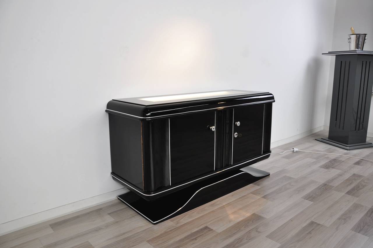 Illuminated Art Deco dresser from the 1940s. Beautiful piece of furniture with a illuminated milk glass plate on top and a matt white interior. It offers wonderful rounded corners and out signature black paintjob with a high gloss finish. Second