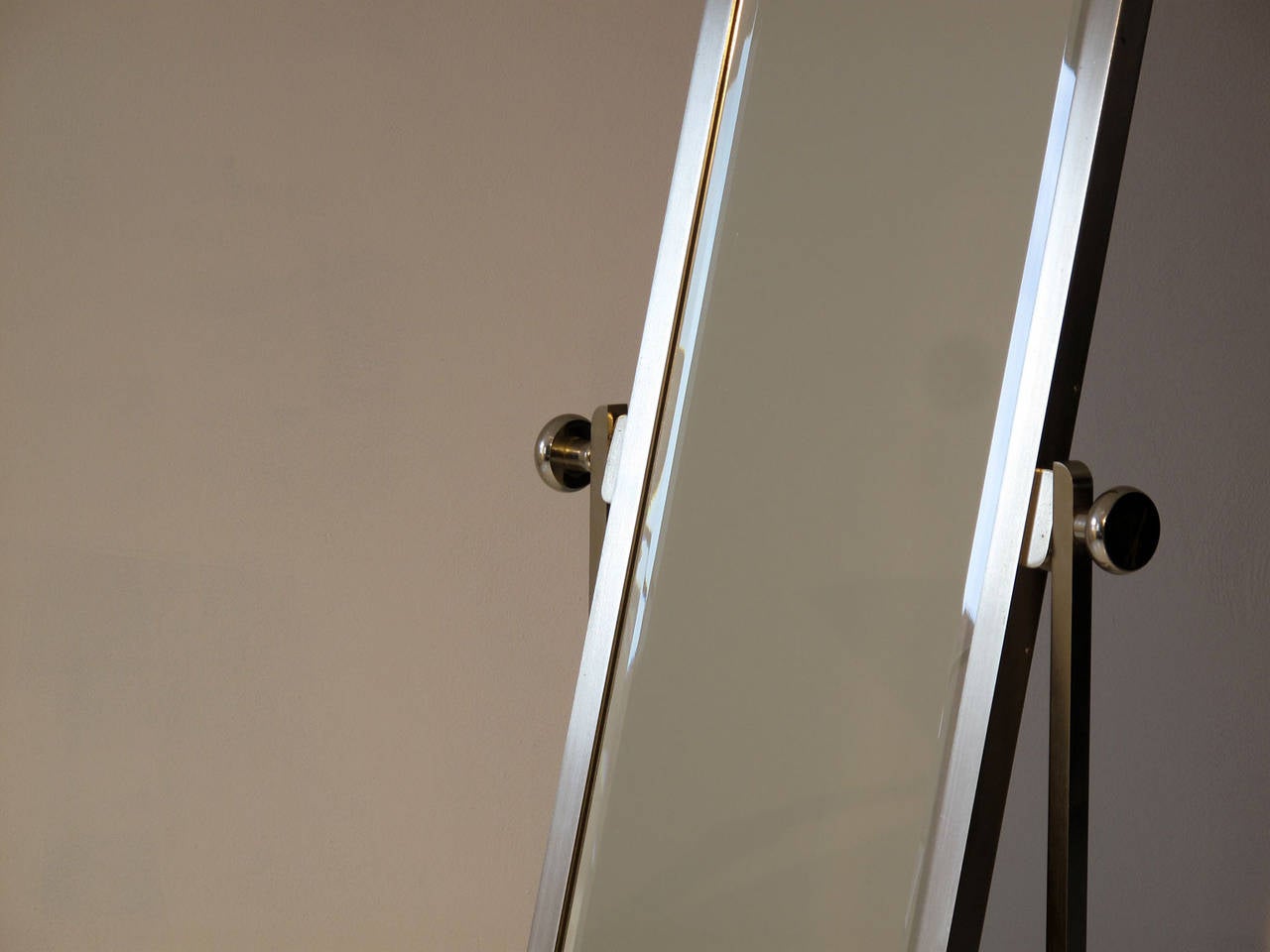 Mid-Century Modern, 1950s aluminum frame standing mirror.
The old brass coating to the aluminum has almost vanished, leaving only a thin layer of golden patina on the frame, which gives the metal an almost white golden color. The mirror itself is