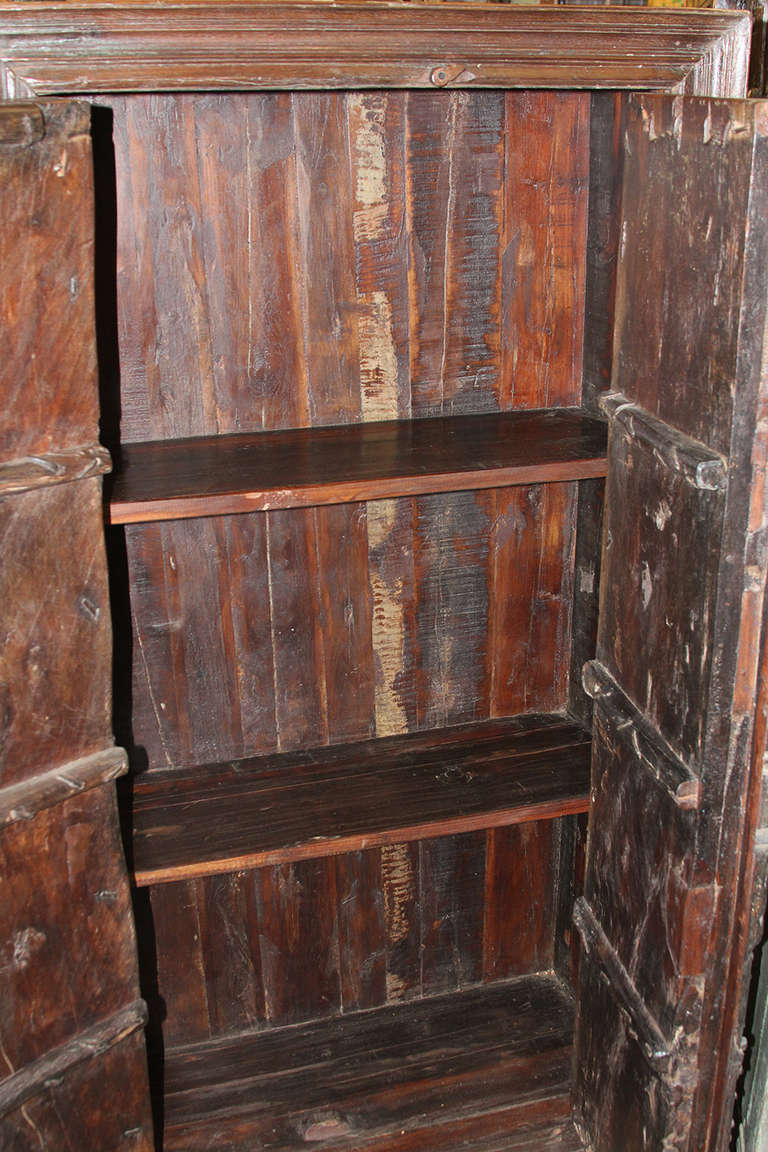 This an antique Burmese teak cabinet with 19th century doors and recycled wood sides and top.  The doors are amazing with great highlights plus acanthus leaf motifs, metal edging and pins on the door frame.  The door handles are also original 19th