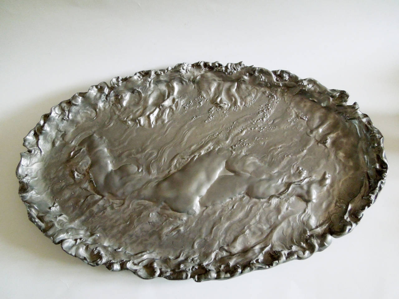 A large oval pewter plaque in deep vigorous relief by the sculptor Jules DESBOIS. The central element being a floating full female nude surrounded by waves.
This model was exhibited at the 1896 Salon de Mars in Paris, and was illustrated by La