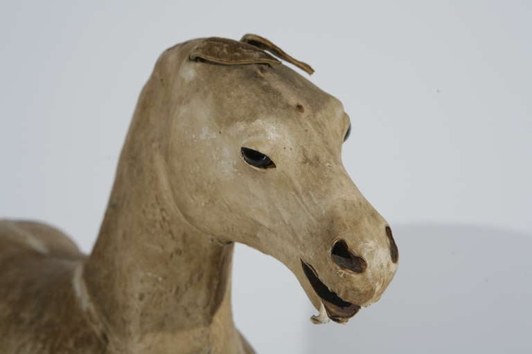 A toy horse with a hair-on-hide leather body and glass eyes.  The body is carved pine, sheathed in cow skin with only partial fur remaining,  Basically the skin is parchment with some hair in a very light brown.  The hooves are painted black.  Both