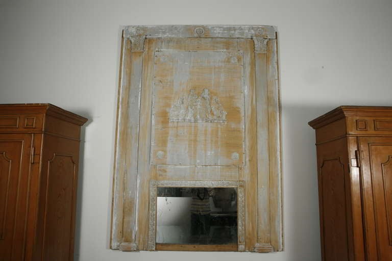 A large wooden trumeau mirror with plaster medallions, capitals and a pastoral scene at the center. Original mirror at bottom. Wood coming through faded paint grey-blue paint.

An outstanding and impressively sized piece.

French, circa 1800