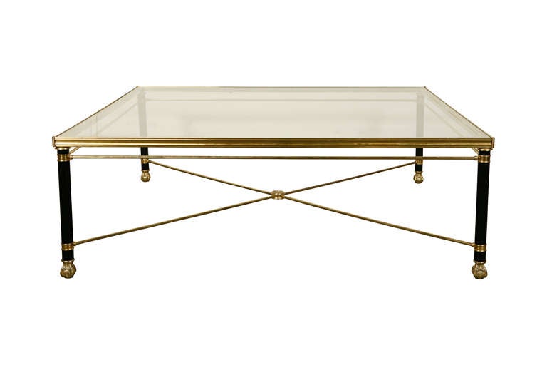 A very large square brass coffee table with claw feet and glass top.
