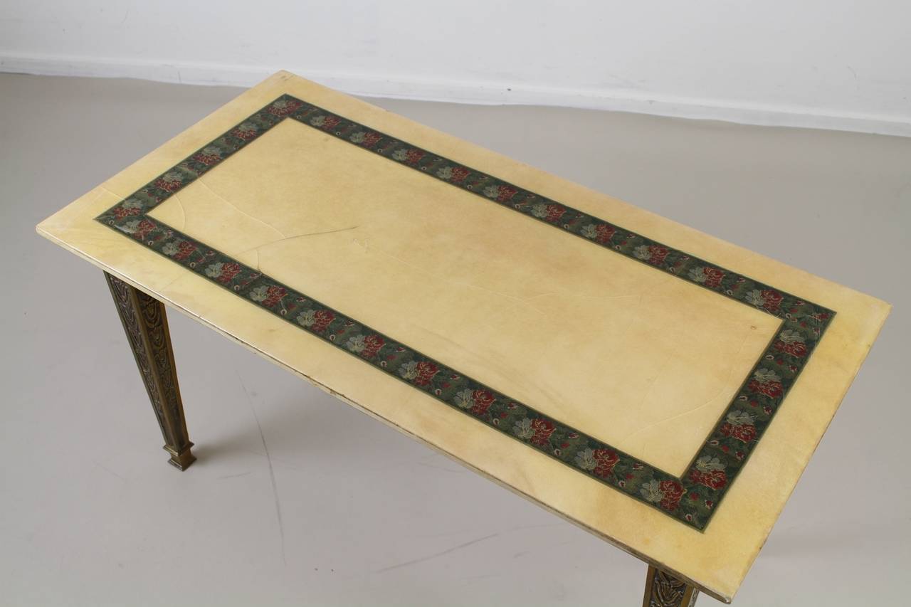 Brass base coffee table.
Lacquered goatskin top with flower stitched inlaid edge.

