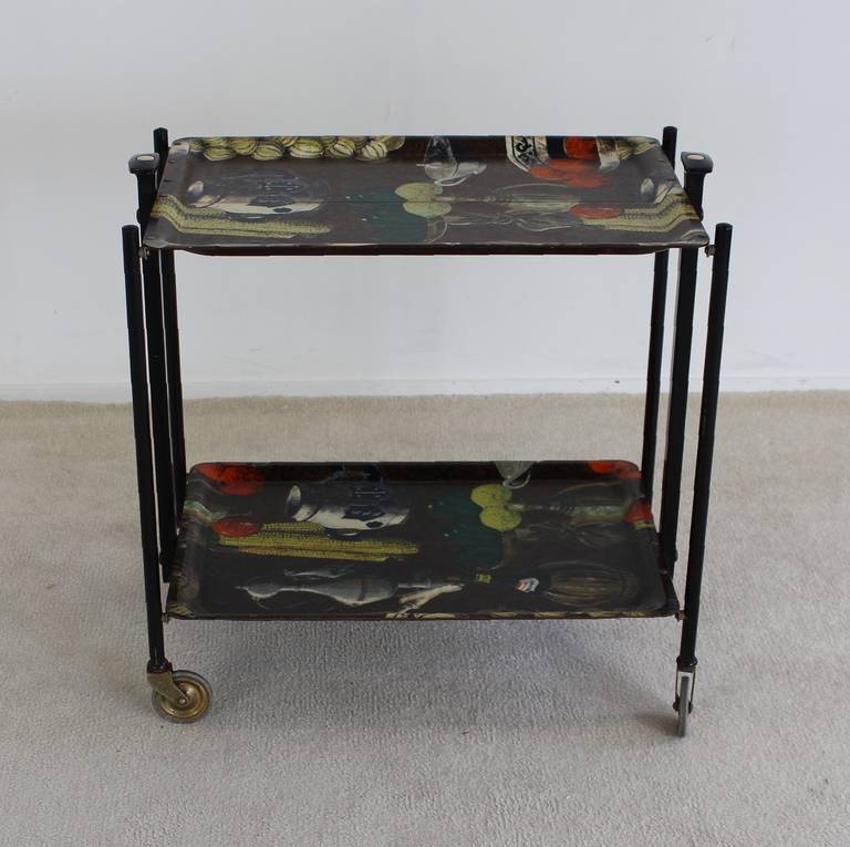This in Fornasetti style decorated serving trolley was produced by Bremshey Gerlinol Germany
Formica shelves on a black steel frame.
Brass details and a collapse mechanism for folding the cart.

Standard shipment advised