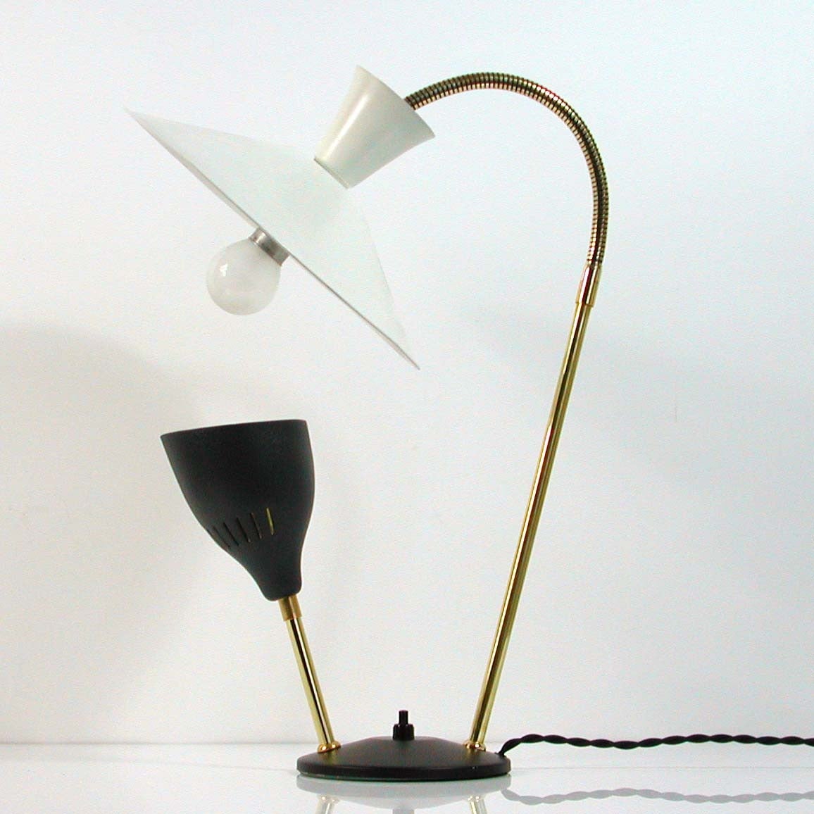 Awesome 1950s double arm brass and metal table lamp by André Lavigne for ALUMINOR Nice France.
The lamp has got one white lacquered lamp shade with goose neck lamp arm and one dark grey lacquered shade on black lacquered base.
Each shade requires