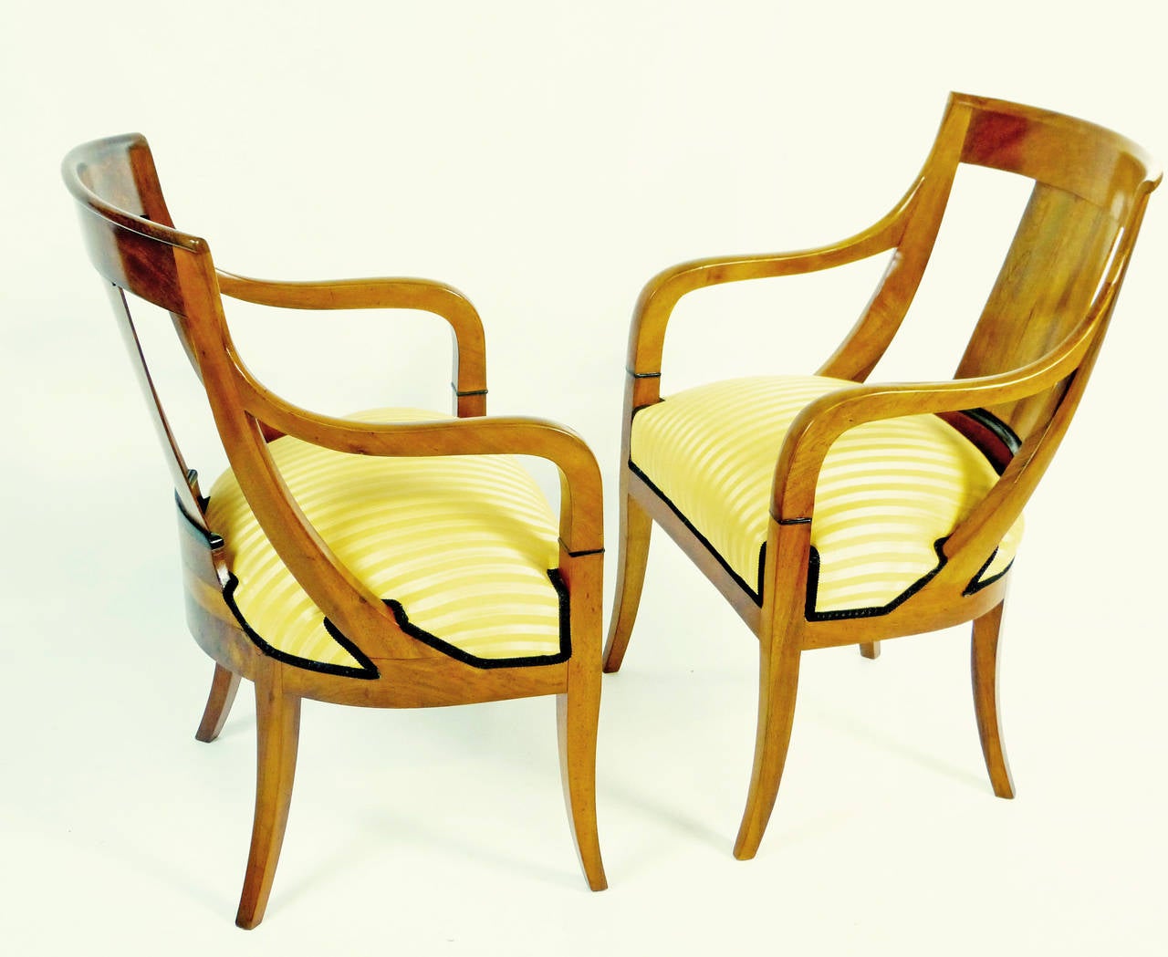 Elegant and unusual pair of period Biedermeier armchairs of north German origin of amber colored solid figured walnut. The supports on each side of the curved back splat unite with the arms and both unite around the top of the front legs to produce