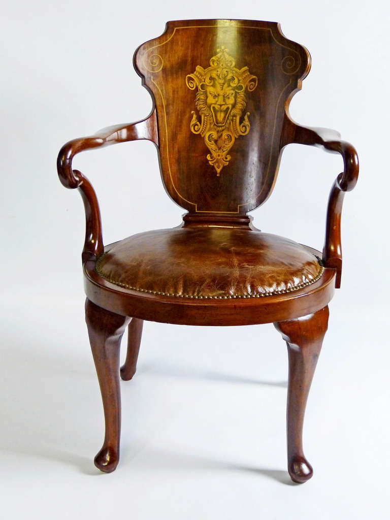 Exquisite mahogany captain's armchair of the English Edwardian period, with oval seat upholstered with distressed leather and cabriole legs in the Queen Anne style. The back splat features an impressive inlaid heraldic lion head that is finely