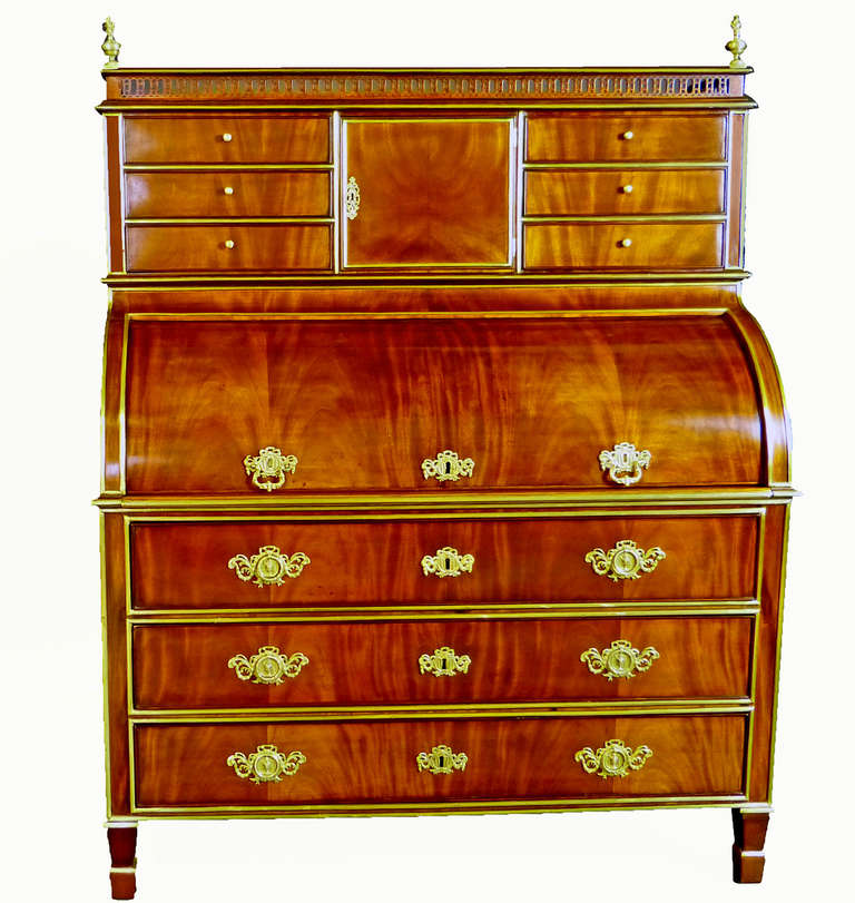 Fine late 18th century figured mahogany cylinder top bureau-secretaire of Russian origin bearing gilded brass linear brass mounts and intricate mahogany fretwork gallery top with brass flame finials. The top 6 drawers flanking a central cupboard are