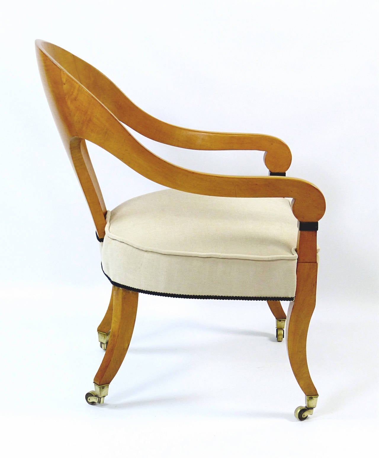 Outstanding armchair of the first Biedermeier period of German origin, created out of solid figured maple with beautifully curved back and arms ending in ebonized highlights and with sabre shaped legs terminating in brass casters. This is certainly