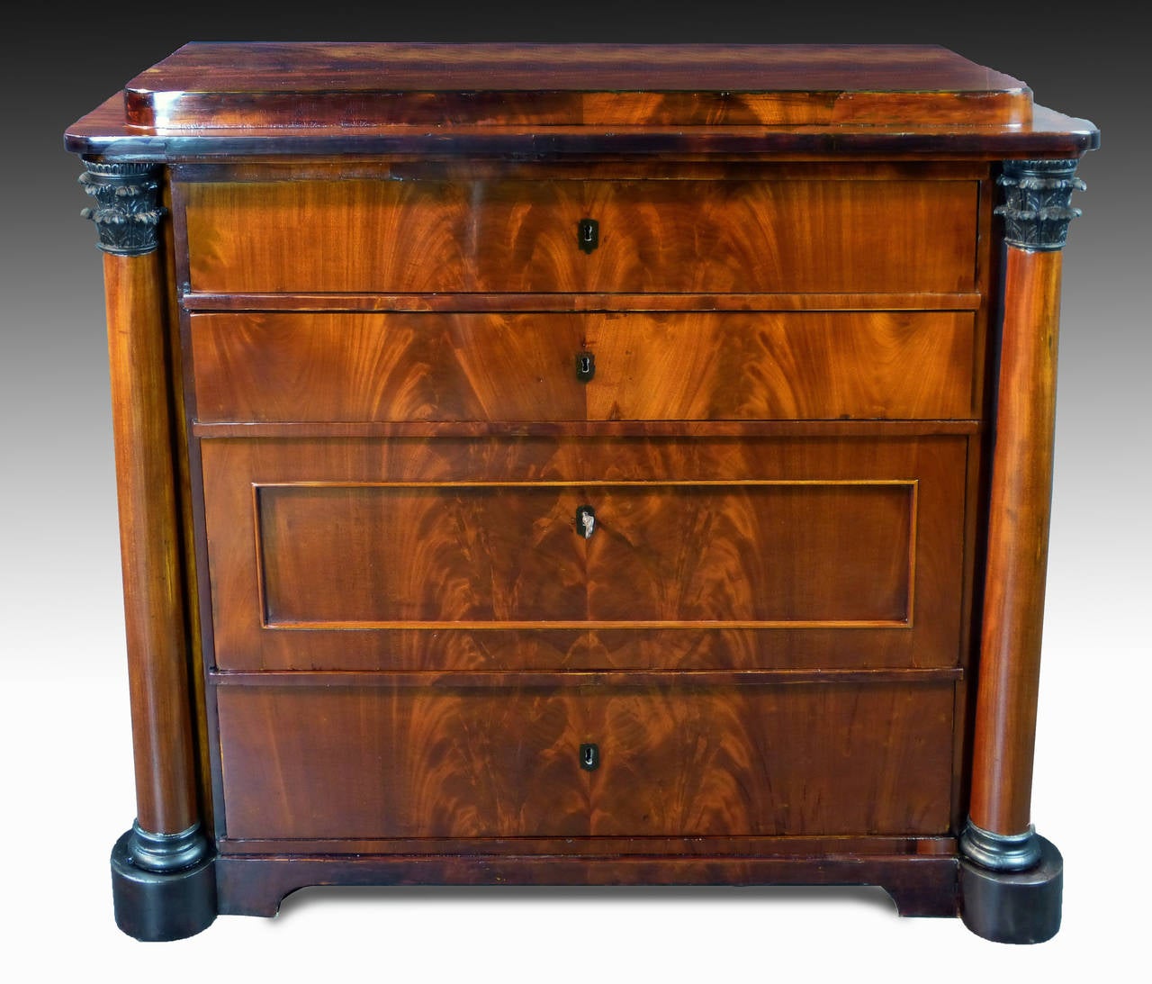 Early Biedermeier figured mahogany commode of Danish origin dating to the first quarter of the 19th century with two Corinthian columns flanking four drawers. The columns have Corinthian tops and bases that are carved wood and are ebonised. Three of
