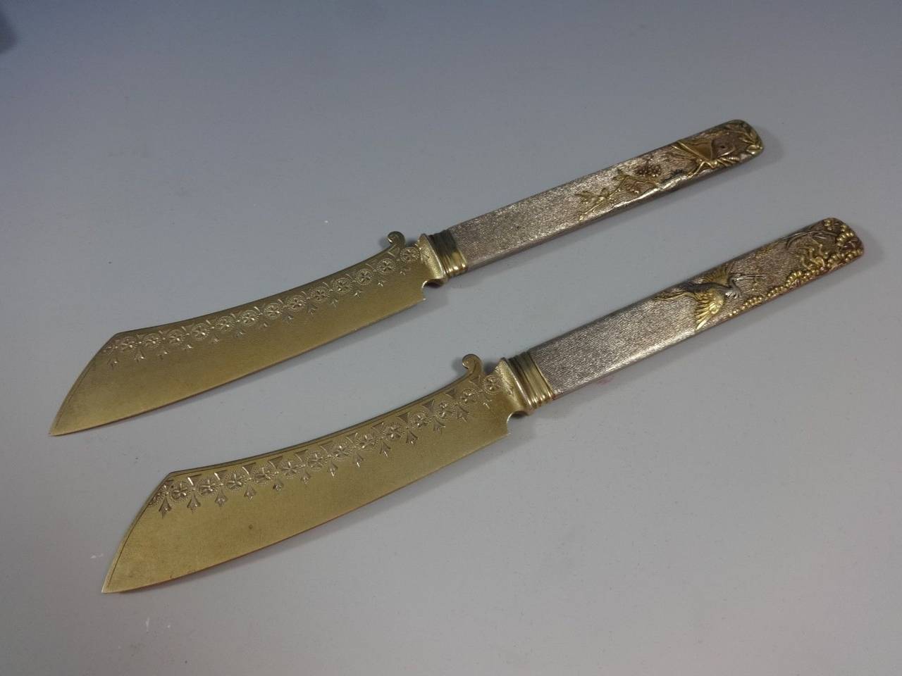 Museum quality pair of mixed metals cheese knives made by Whiting with applied elements, 7 ½” - One with gold and copper butterfly motif, the other with stork and young motif. Brite-cut engraved blades. Given as 50th wedding anniversary gift in the