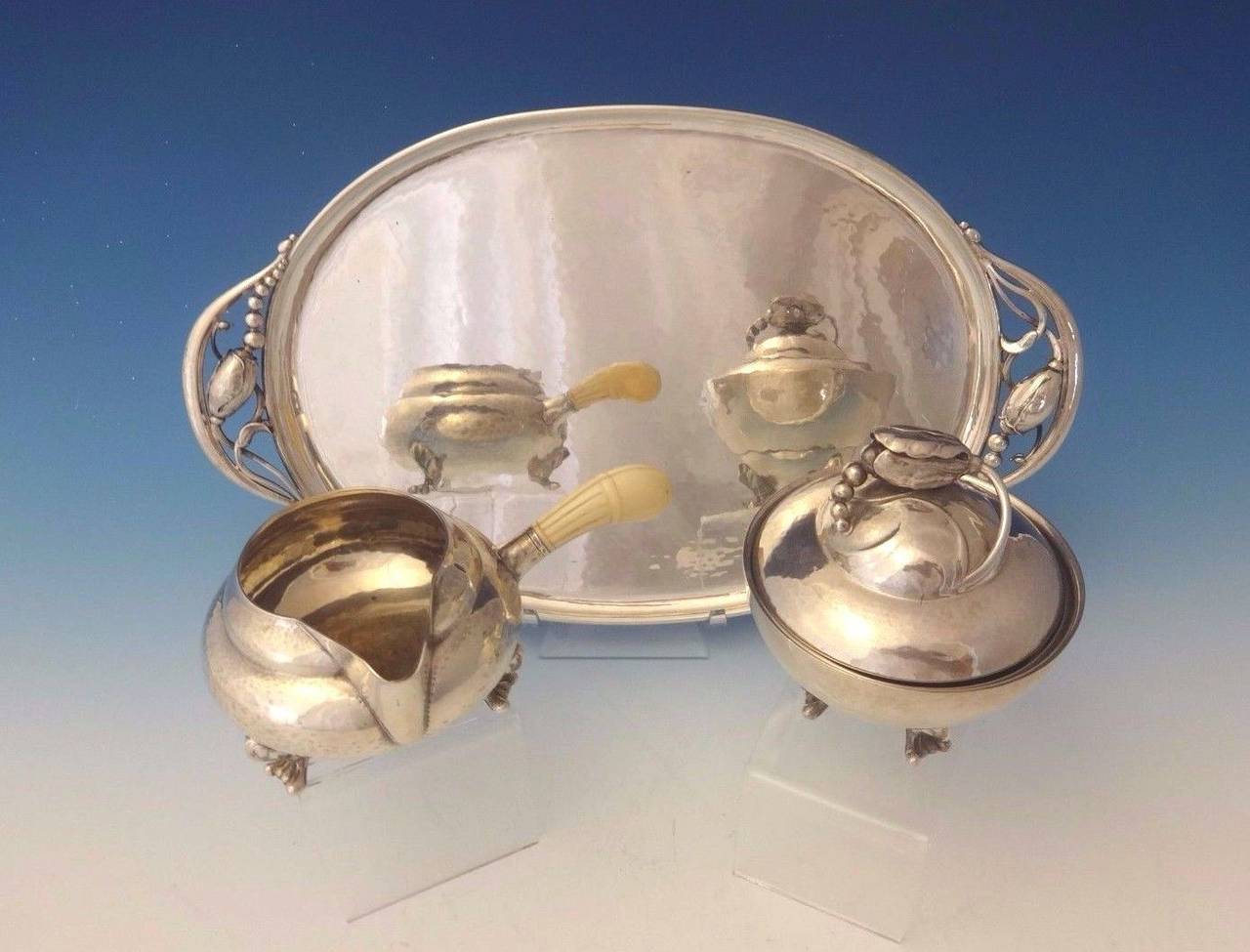 Blossom by Georg Jensen.
This exquisite Blossom by Georg Jensen sterling set includes a sugar bowl, creamer, and a tray with date marks circa in the 1950s. 

Tray: 14" long, 8 1/4" wide, weighs 19.4 ozt and marked with #2H. 
Creamer: 2