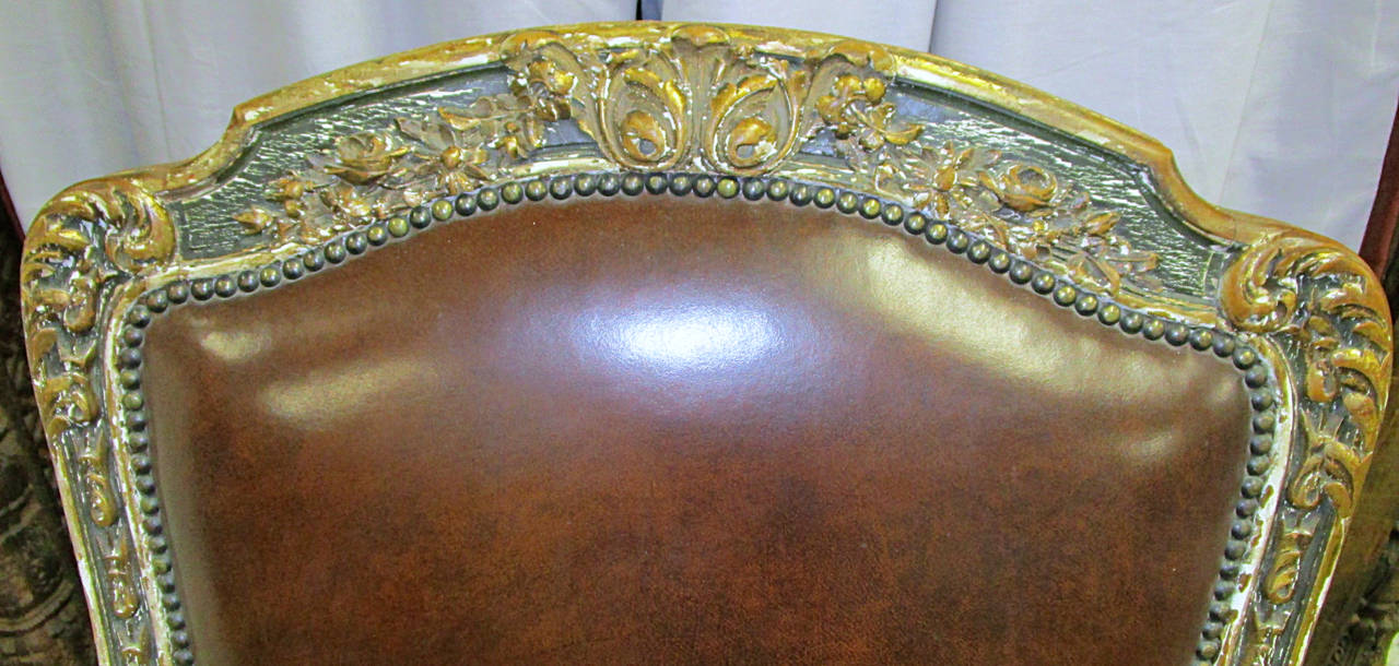 A wonderfully carved chair in worn green paint and parcel-gilt. Upholstered in a rich dark chocolate supple leather complete with nailhead trim.