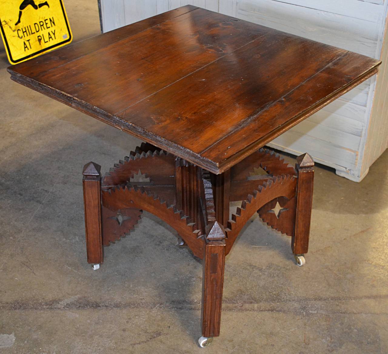 A wonderful example of late 19th century folk art in furniture. Four board pine top joined on angled cuts. Fluted square column pedestal supported by arched stretchers with rickrack details joined to four square posts with pyramid finials and
