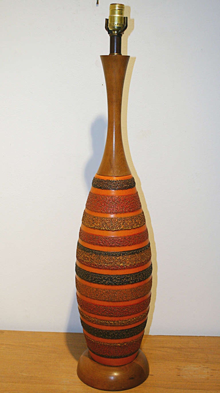 Bottle shaped wood and ceramic lamp. Neck and bass in walnut. Body of lamp is ceramic consisting of alternating rings of raised multi color crater glazed wide bands and narrower orange crackle glaze bands. 34