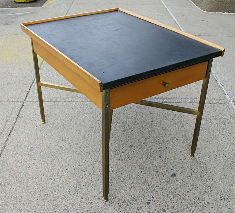 A Milo Baughman designed occasional table for Murray Furniture. Black leather top wrapped over a maple case with drawer is supported by square brass legs and cross stretcher. All adjustable leveling feet present.