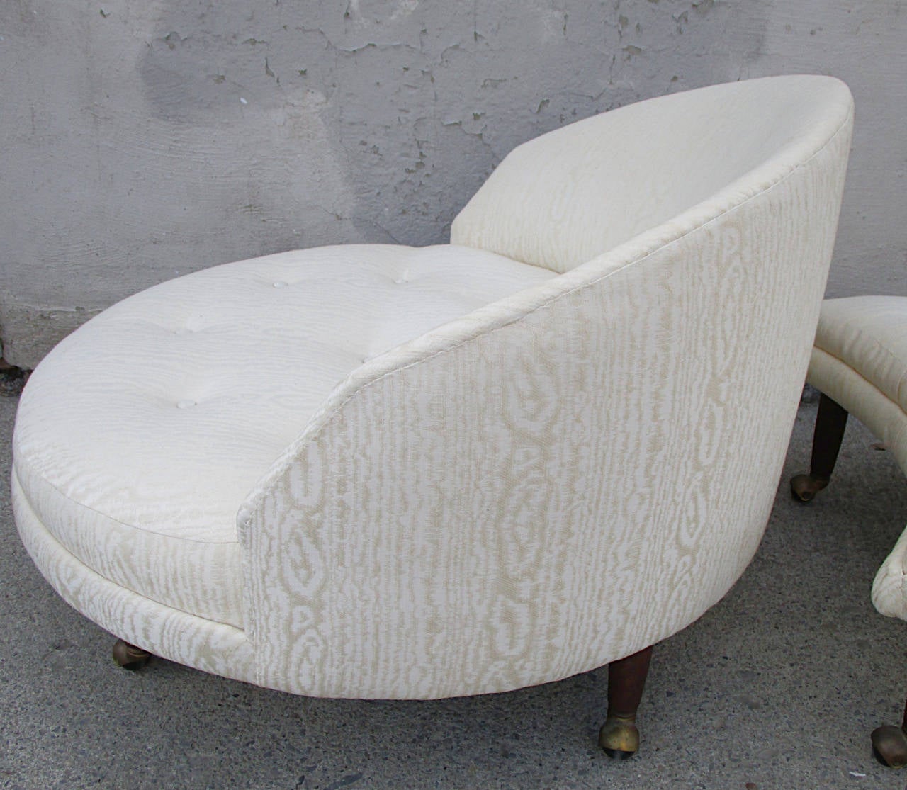 Round lounge chair with crescent ottoman. Turned tapered walnut legs on brass and black casters. Most likely reupholstered in the late '80's in cream moire. Button tufted seat and otto top.This upholstery is in excellent condition.  However,