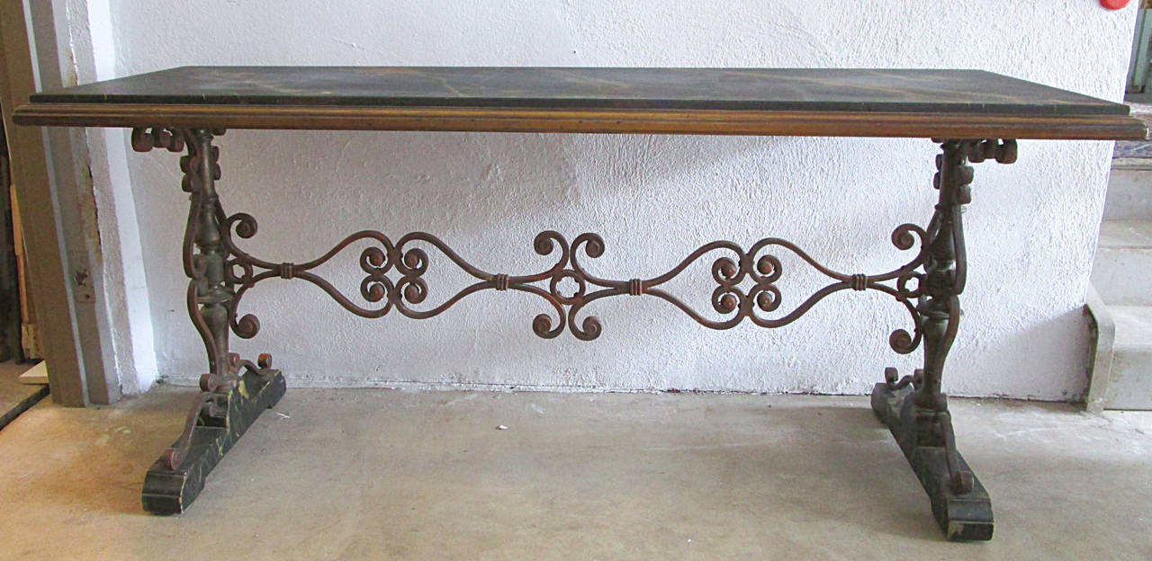 A double pedestal console in the Spanish revival taste of the early 20th century. The top consists of a painted faux marble counter in hues of greens and oranges on a black background with an aged burnished gold trim molding. Top has achieved a fine