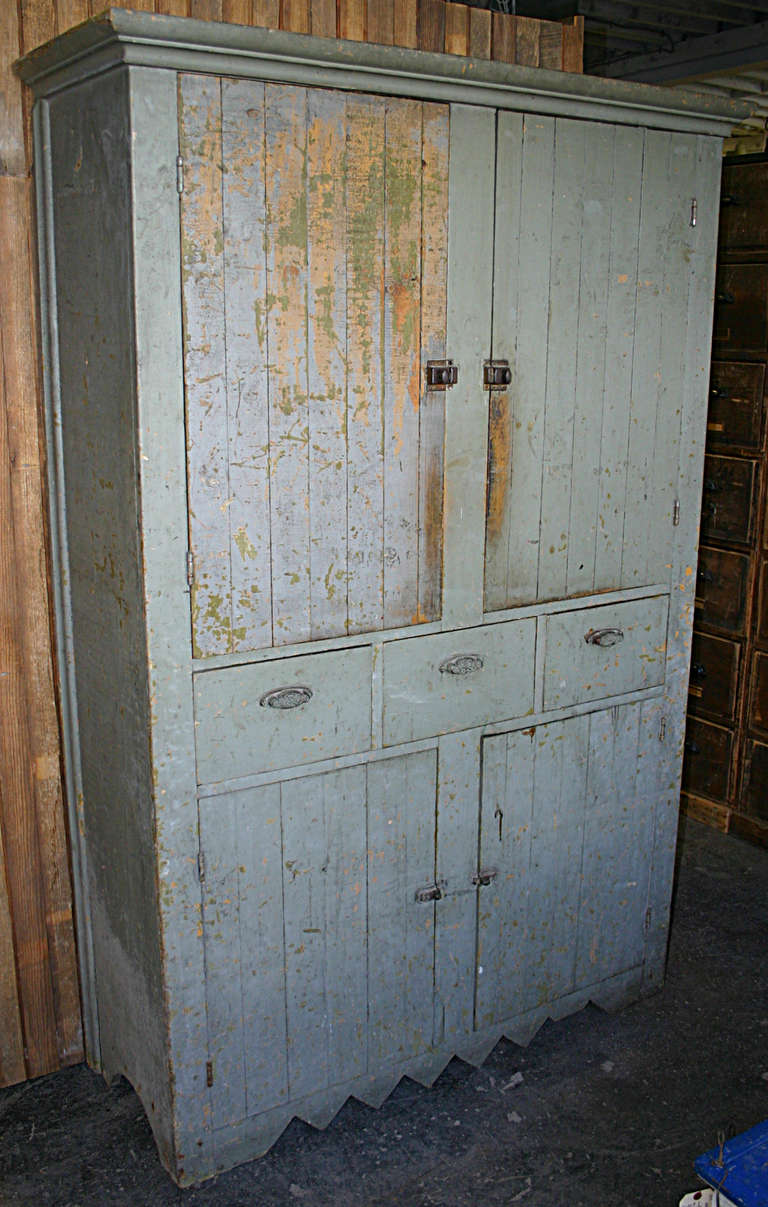 Beautiful farm cupboard in hues of grey blue and green, all original. Ogee crown over four planked doors separated by mid row of three flat front drawers home to cast bin pulls. Doors have spring twist surface catches. Base detail has arches on