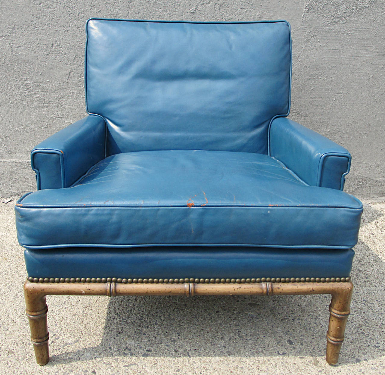 Club chair by Erwin-Lambeth for John Stuart. Worn appropriately, this blue leather chair sit extremely comfortably. Faux bamboo legs are reminiscent of Robsjohn-Gibbings chairs of the same period. Wear to finish on feet.