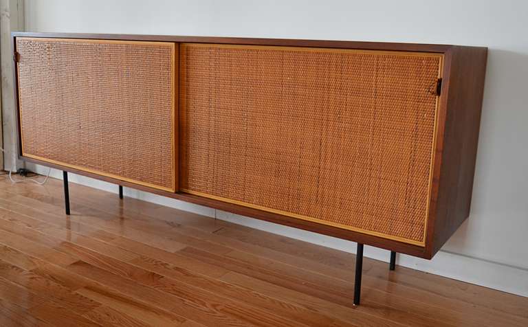 An early example of a Florence Knoll's contribution to the Knoll line. Walnut case with two sliding cane front doors. interior divided into three compartments, two with adjustable wood shelves and one with pull out divided felt lined drawer and