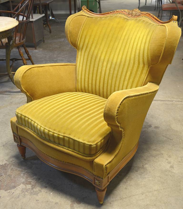 A wonderful stylized wing chair with beautiful lines. Original gold mohair body with similar gold striped mohair on interior back and seat. Carved crest with gold painted accents. Unique brass star details and brass sabots with ball detail under