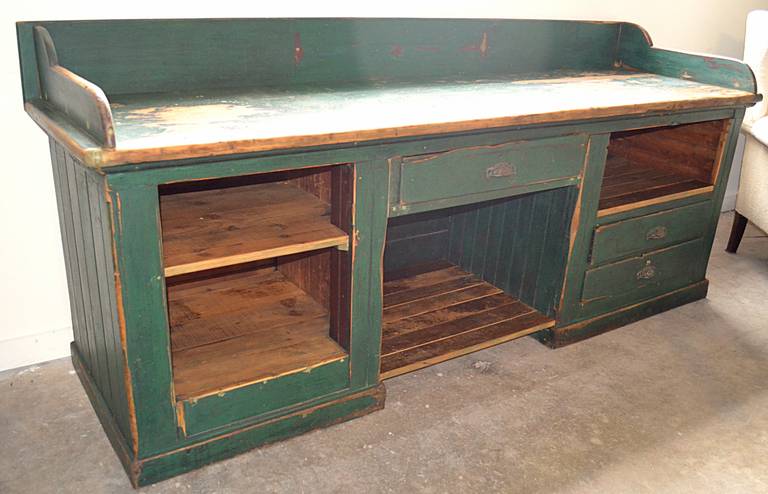 Old work bench or store counter with gallery. Old distressed green paint on all outer surfaces. Heavily worn on counter. Open cubbies and three drawers with cast bin pulls. counter height is 32"