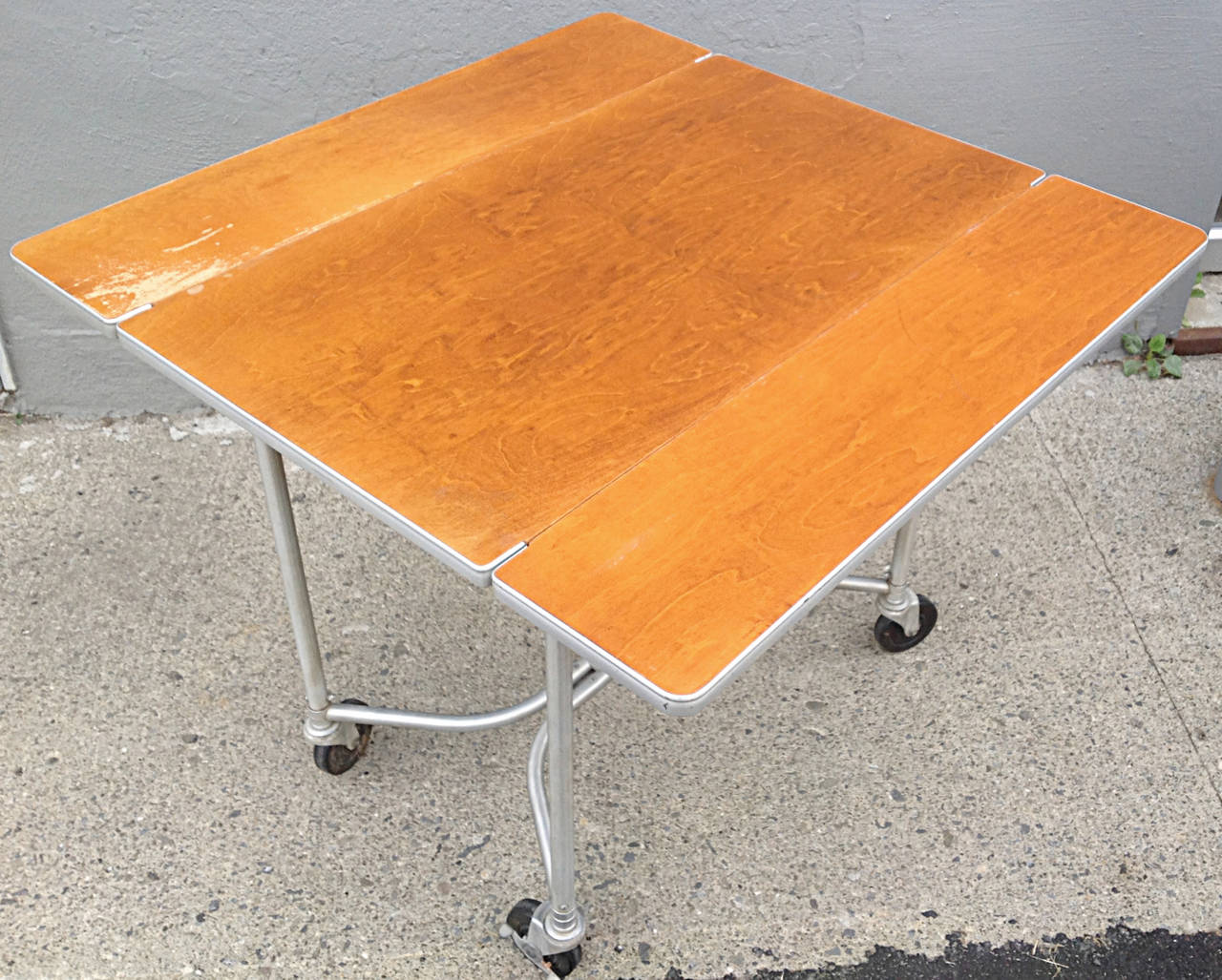 Fantastic 1930's aluminum and birch drop leaf rolling table by Warren McArthur. Classic Aluminum tube framing with signature McArthur hardware. Large heavy rubber locking casters. Original finish and warm patina to birch top. Aluminum edge banding