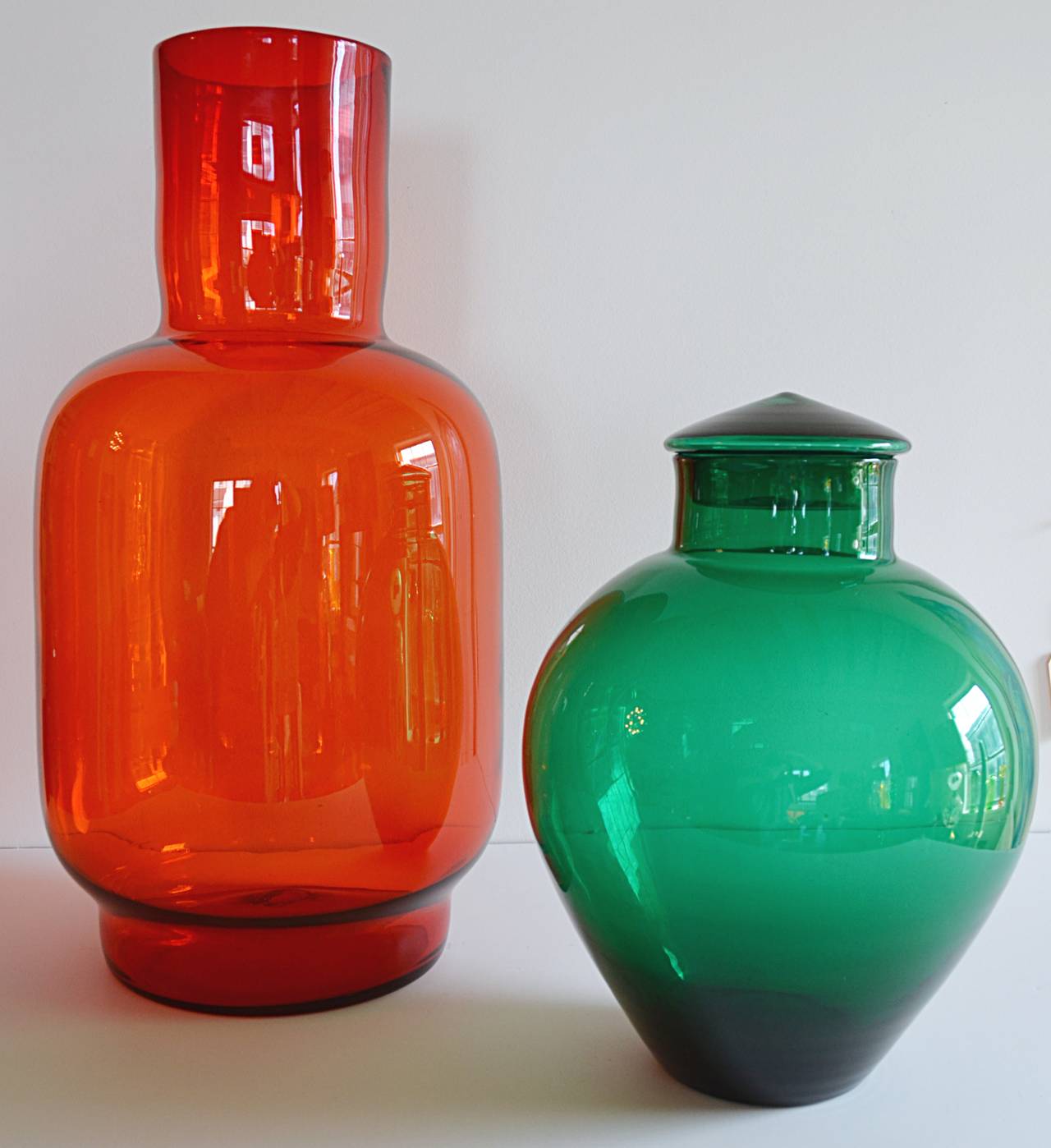 A two-piece Blenko blown glass collection consisting of tall tangerine vase and green covered jar. Jar measures 10.25
