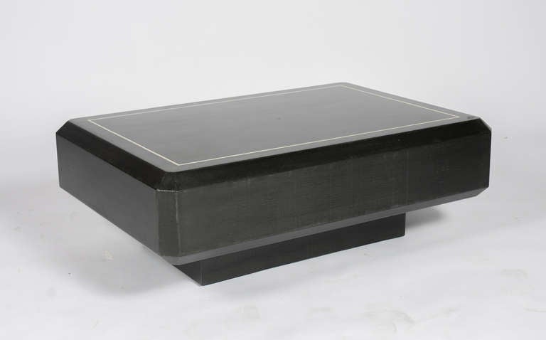 Unusual coffee table by Karl Springer Ltd., circa 1970s. The faceted rectangular top is covered in lacquered black linen fabric with a bone inlay border. The recessed pedestal base is illuminated by four concealed lights. This item is in our