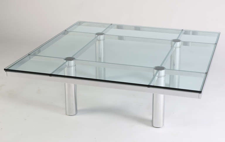 Iconic Andre coffee table.  Distinctive intersecting supports connect four rounded legs the exterior frame.  The clear glass top is inset into the metal frame and rests on four leather disks covering the top of each leg.