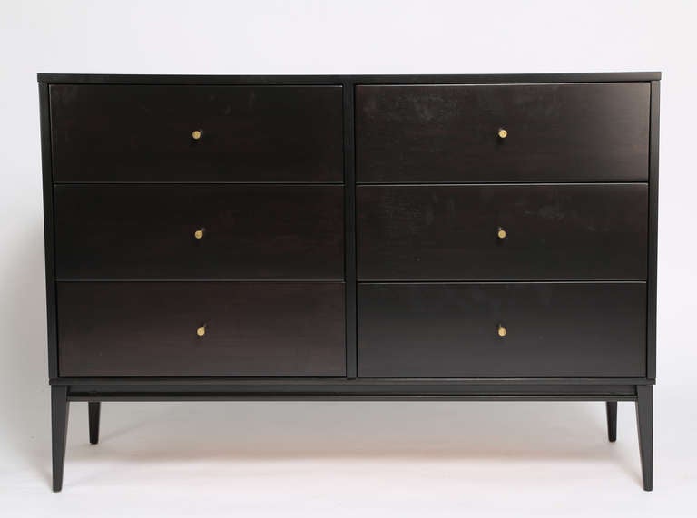 Six-drawer dresser supported by an elegantly tapered leg at each corner.  Original conical brass pulls. The maple has been refinished in a gorgeous hand-applied black satin lacquer. This rich finish allows a bit of the grain to show